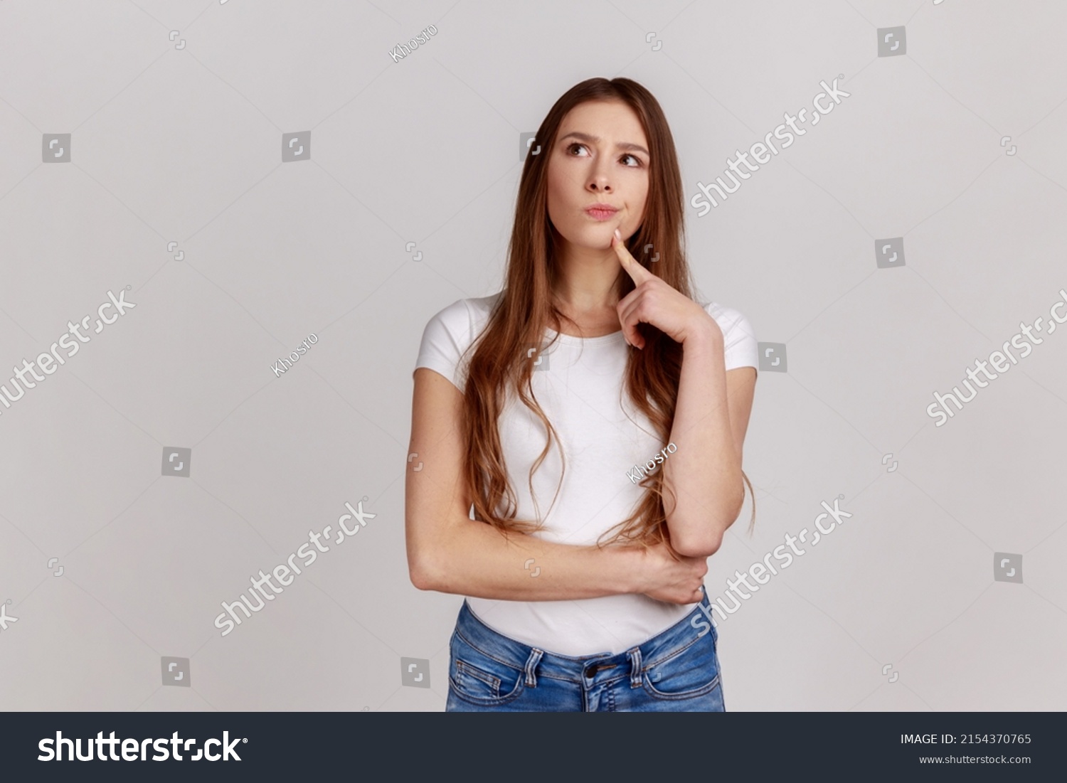 Portrait of standing with thoughtful serious smart expression, pondering answer, having doubts and suspicion, wearing white T-shirt. Indoor studio shot isolated on gray background. #2154370765