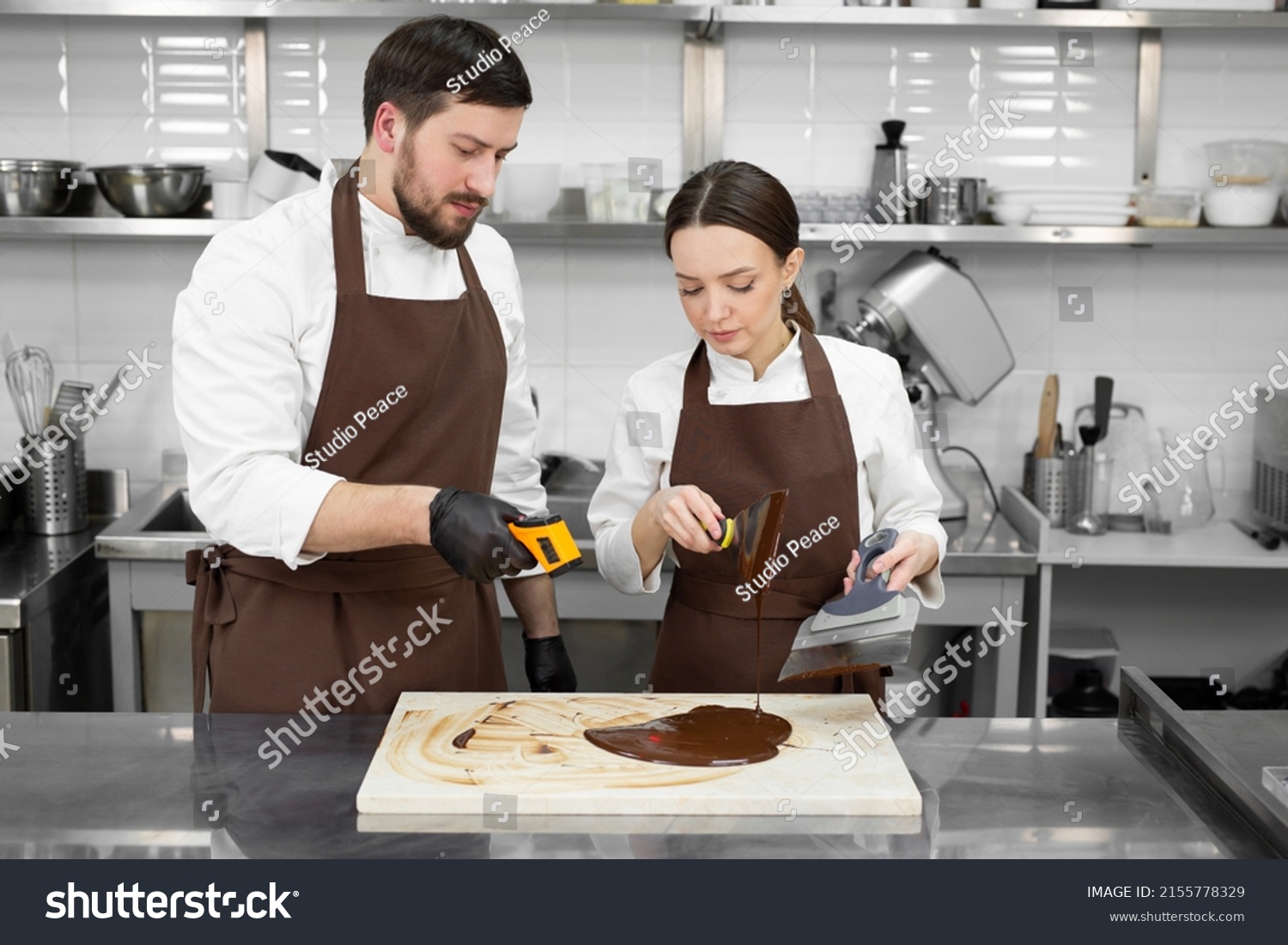 Couple, a man and a woman temper the chocolate and measure the temperature with a non-contact thermometer. #2155778329