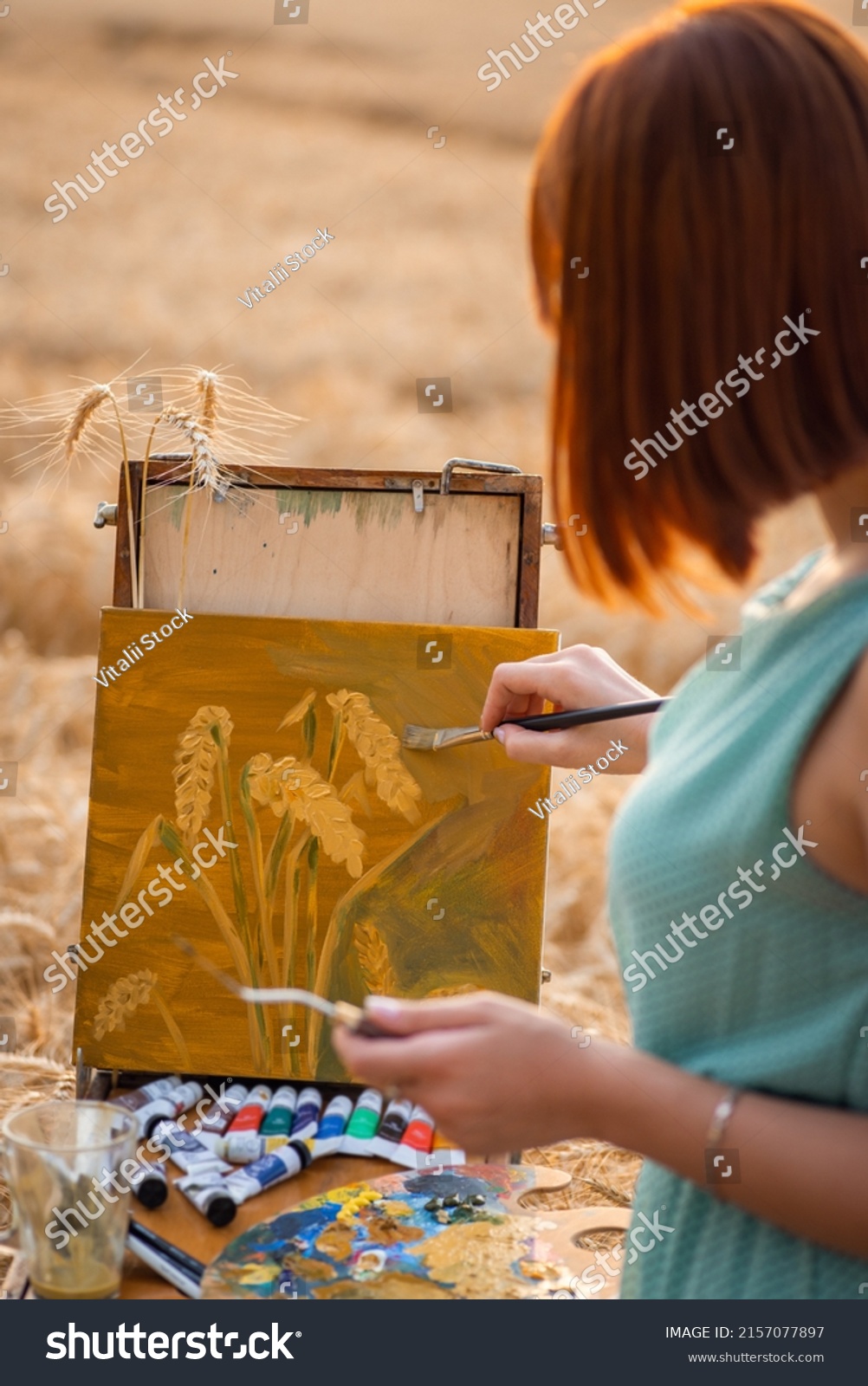 Back view of a girl painter depicting wheat spikelets on canvas. Young girl doing her favourite hobby #2157077897