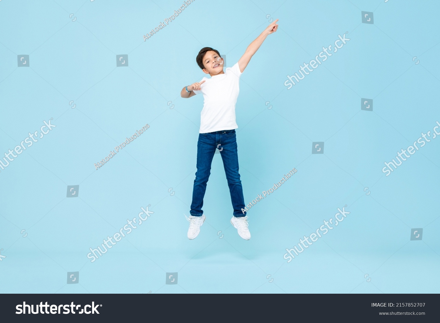 Cute Asian mixed race boy jumping with hand pointing up in isolated light blue color studio background #2157852707