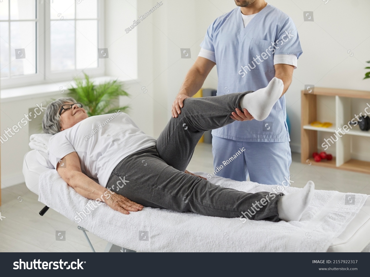 Happy senior woman lying on exam couch while chiropractor, osteopath or physiotherapy specialist is examining her leg and knee. Osteoporosis treatment, physical therapy, remedial exercise concept #2157922317