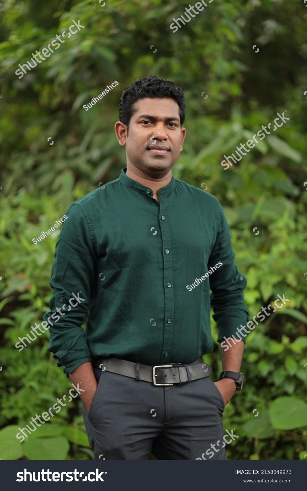 

Young Indian man wearing green shirt standing over green background smiling and looking at the camera  #2158049973