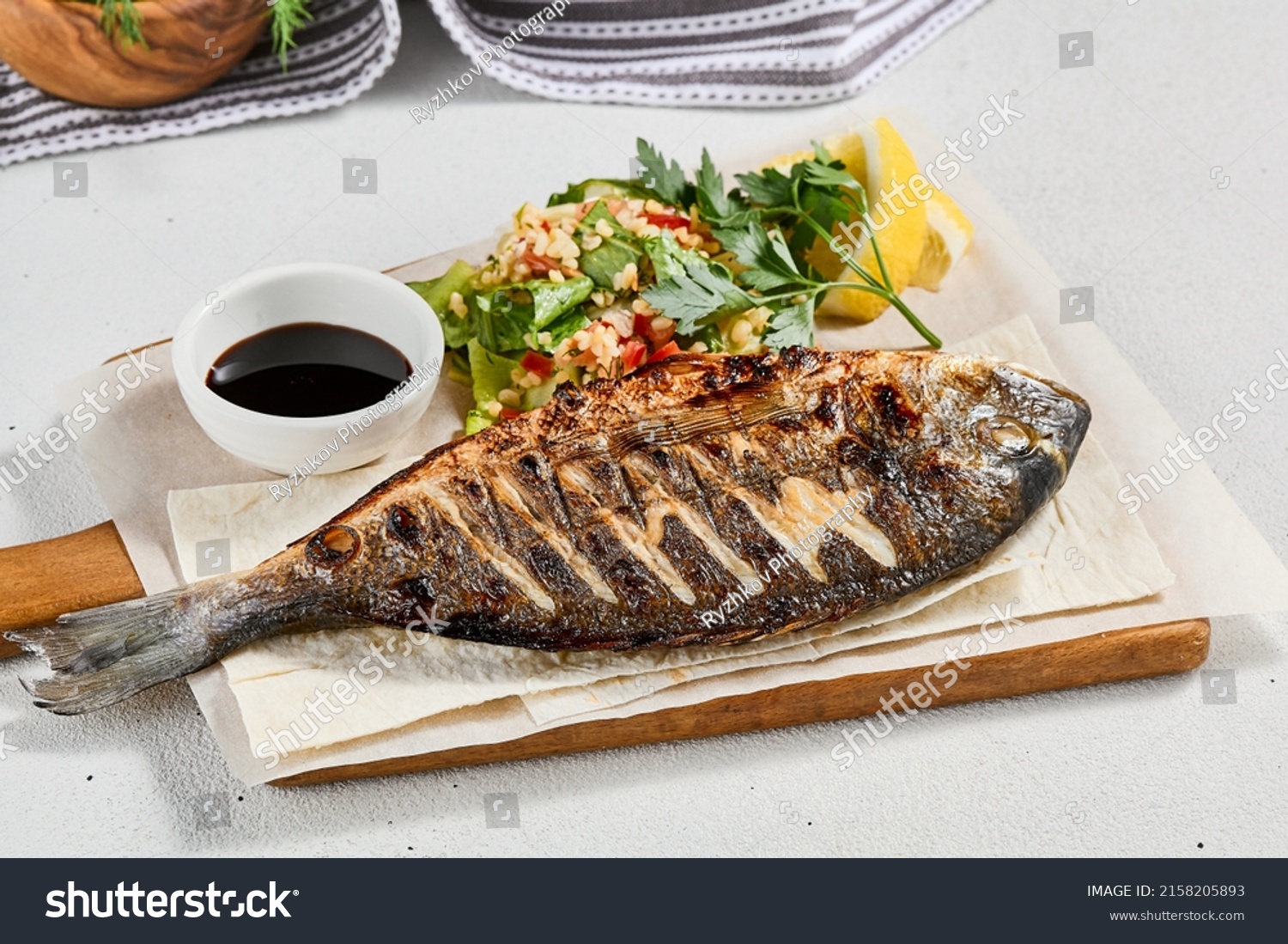 Grilled dorado with garnish on concrete background. Aesthetic composition with bbq fish and vegetables. Healthy food - roasted dorado. Fish dish in minimal style. Whole grilled fish #2158205893
