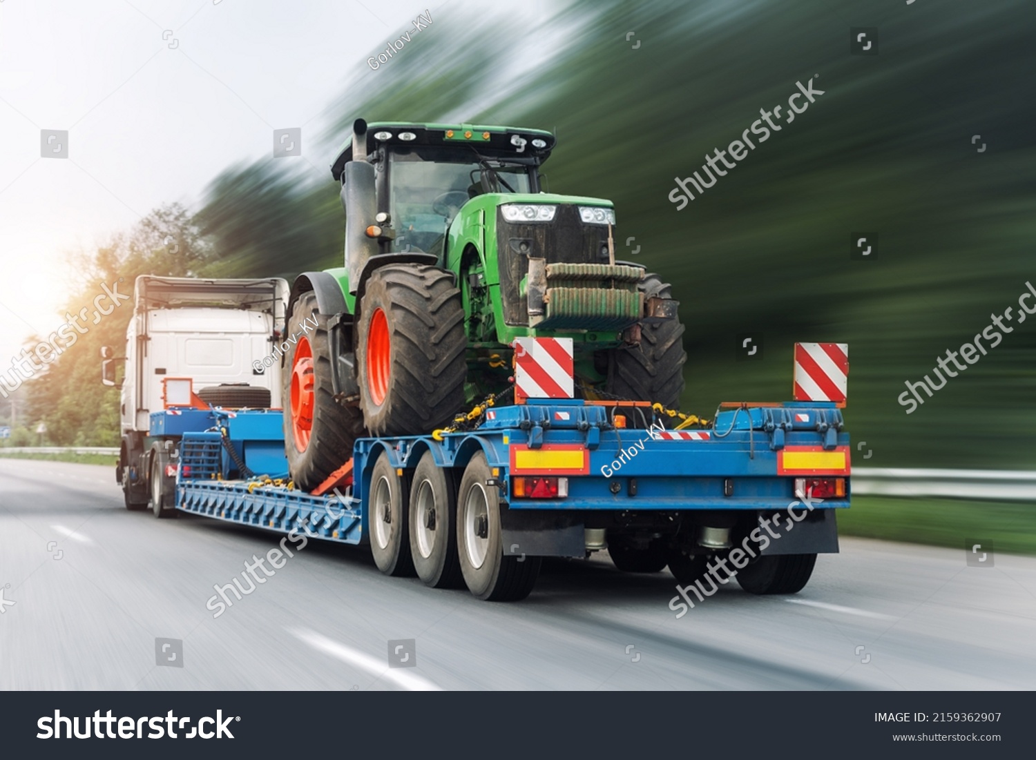POV heavy industrial truck semi trailer flatbed platform transport one big modern farming tractor machine on common highway road at bright day sky. Agricultural equipment transportation service work #2159362907