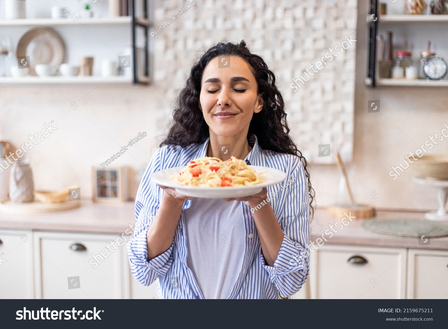 Happy lady tasting homemade spaghetti while having lunch, enjoying the smell with eyes closed, sitting in kitchen interior. Woman cooking and eating tasty food at home #2159675211