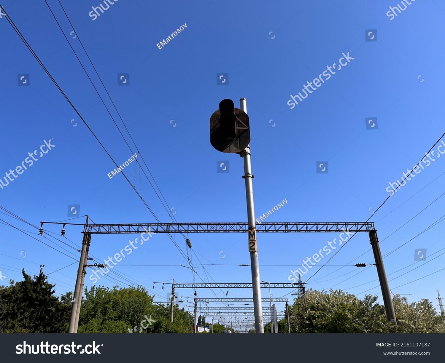 A post with stoplight at the railway station. A stop light mounted on a high pole at the platform against electric wires, powerline and cables #2161107187