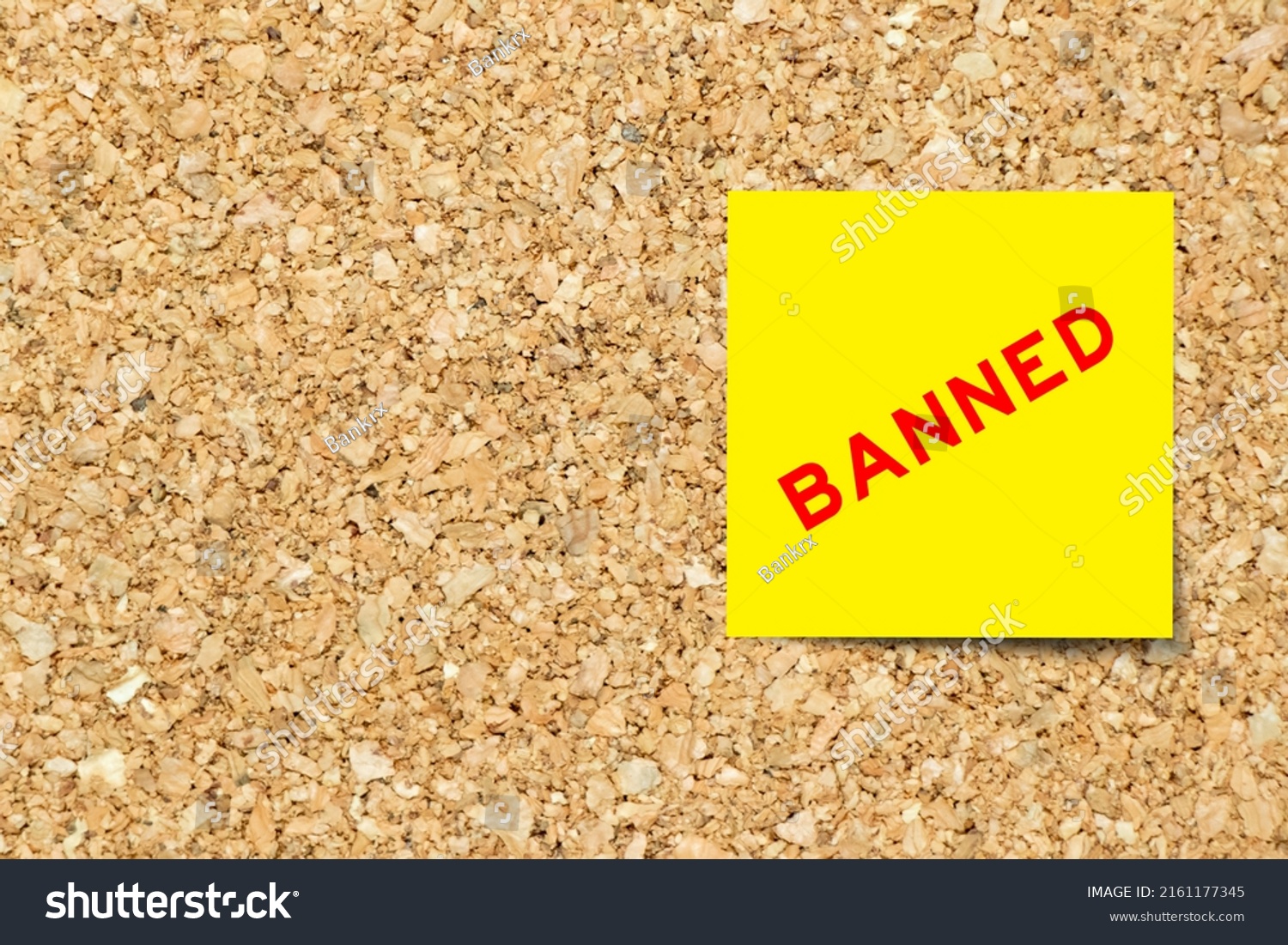 Yellow note paper with word banned on cork board background with copy space #2161177345