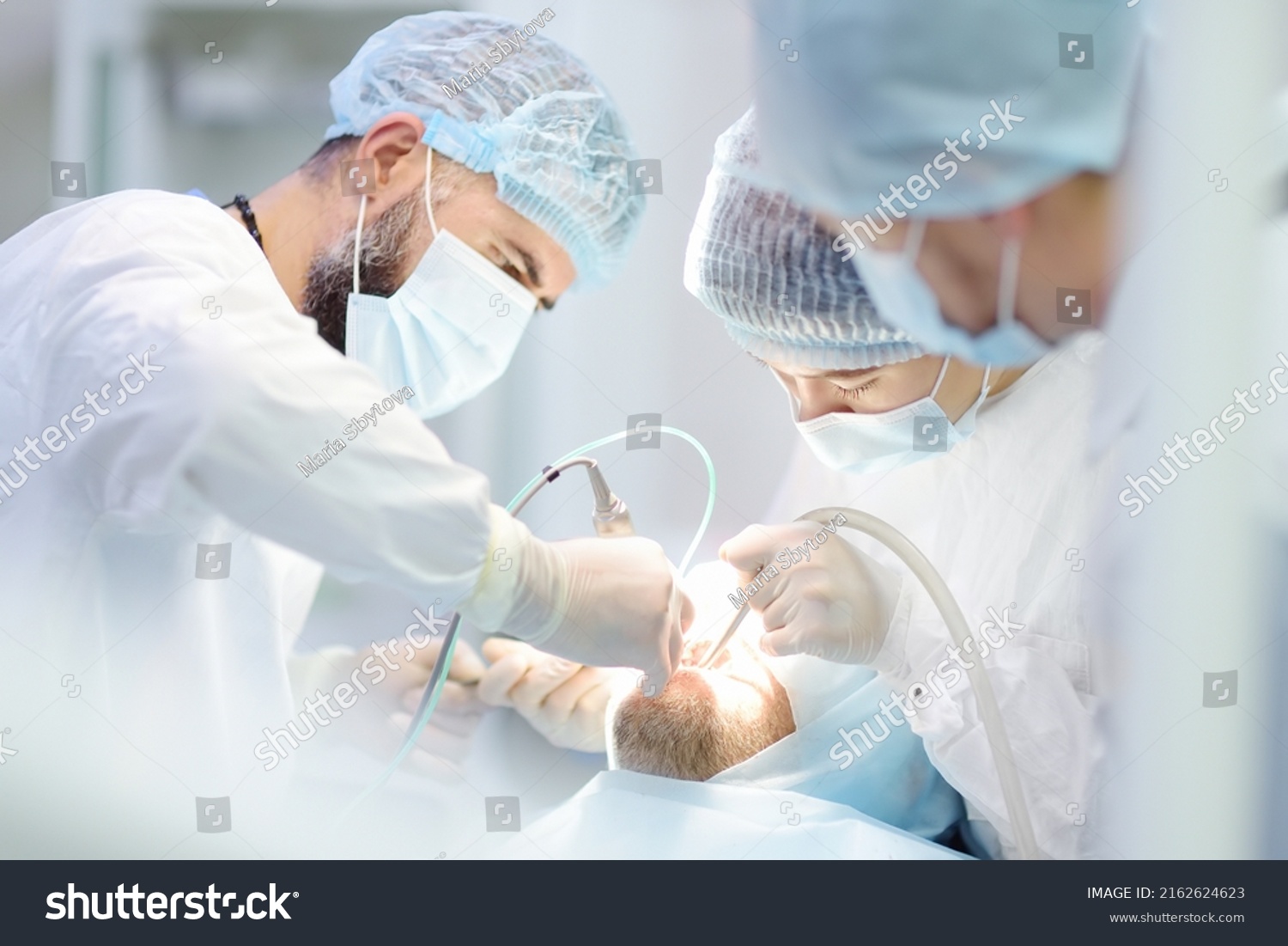 Surgeons and nurse during a dental operation.Anesthetized patient in the operating room.Installation of dental implants or tooth extraction in the clinic. General anesthesia during orthodontic surgery #2162624623