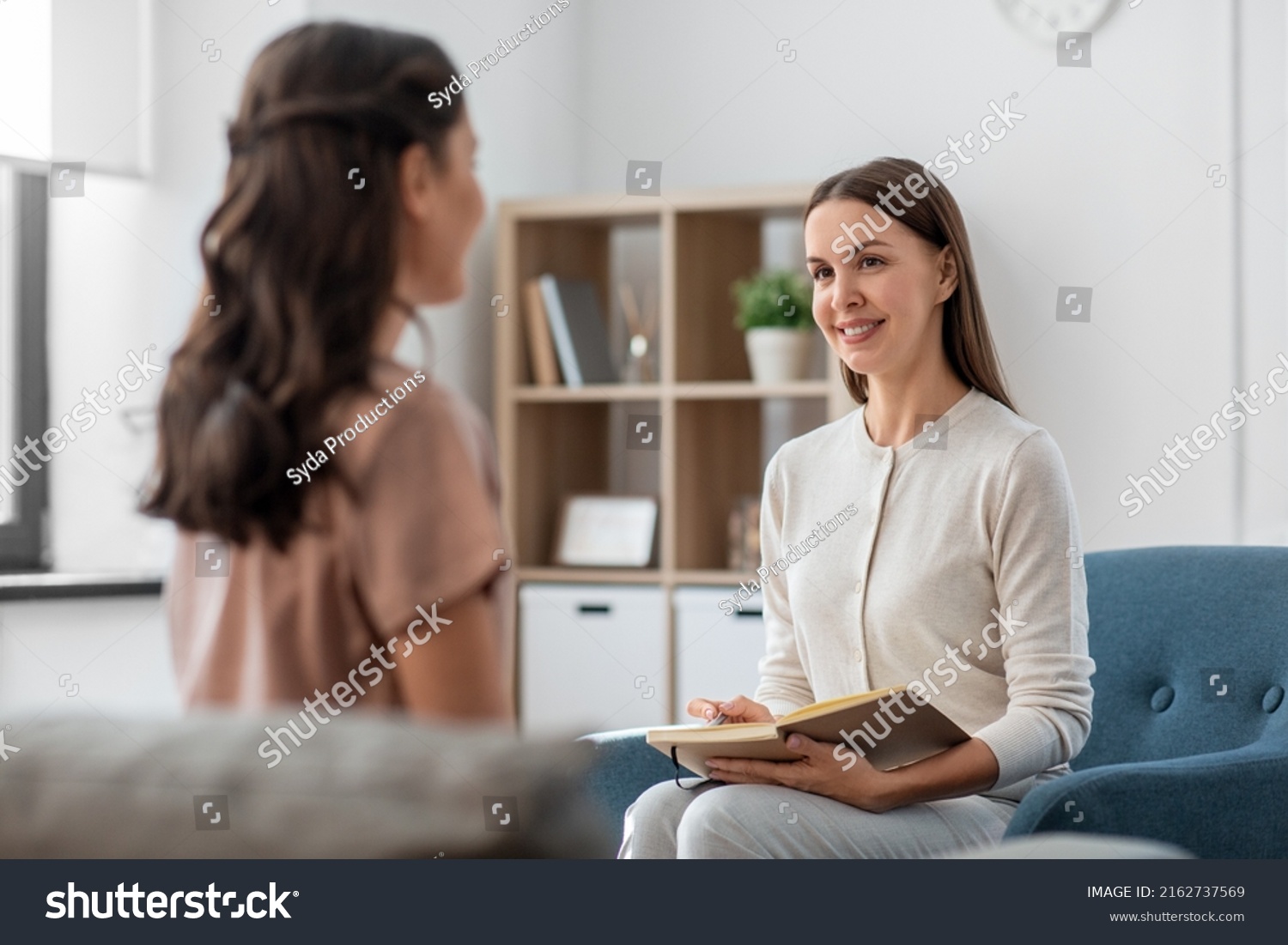 psychology, mental health and people concept - smiling psychologist with notebook and woman patient at psychotherapy session #2162737569