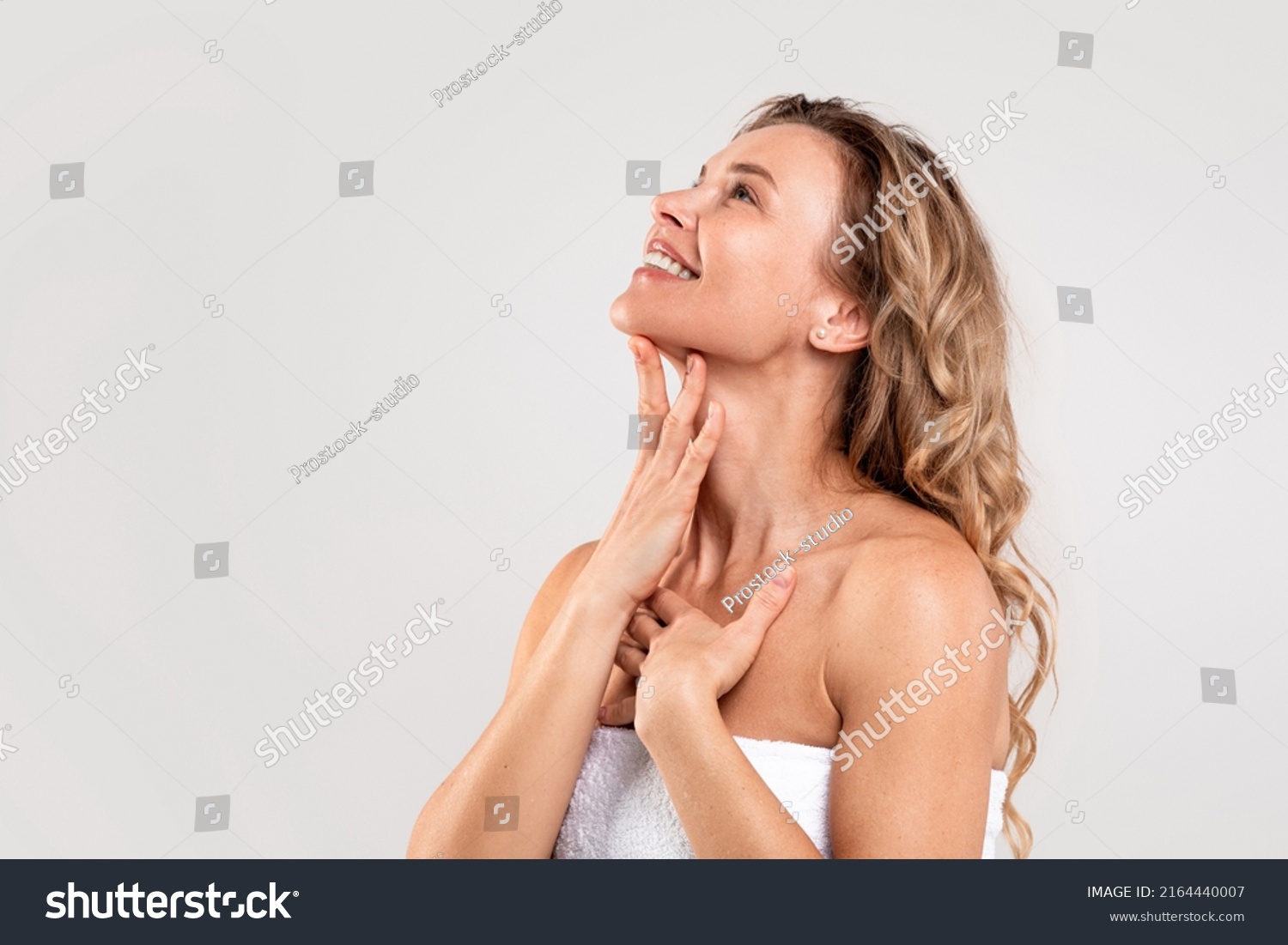 Double Chin Treatment. Beautiful Middle Aged Woman Touching Soft Smooth Skin On Neck, Attractive Mature Lady Standing Wrapped In Towel Over Light Grey Background, Enjoying Her Beauty, Copy Space #2164440007