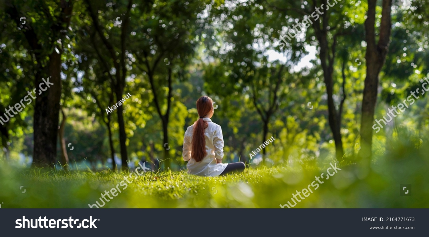 Woman relaxingly practicing meditation in the forest to attain happiness from inner peace wisdom with beam of sun light for healthy mind and soul #2164771673