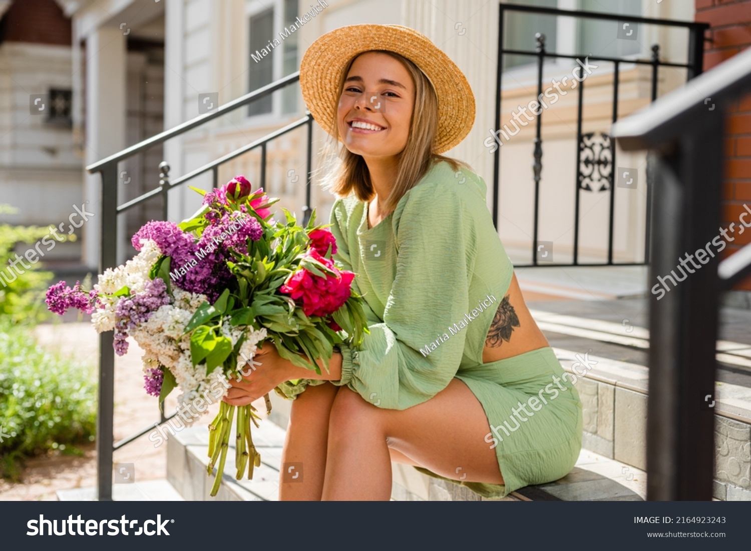 beautiful young woman in summer style outfit smiling happy walking with flowers in city street wearing straw hat fashion trend, sitting on stairs #2164923243