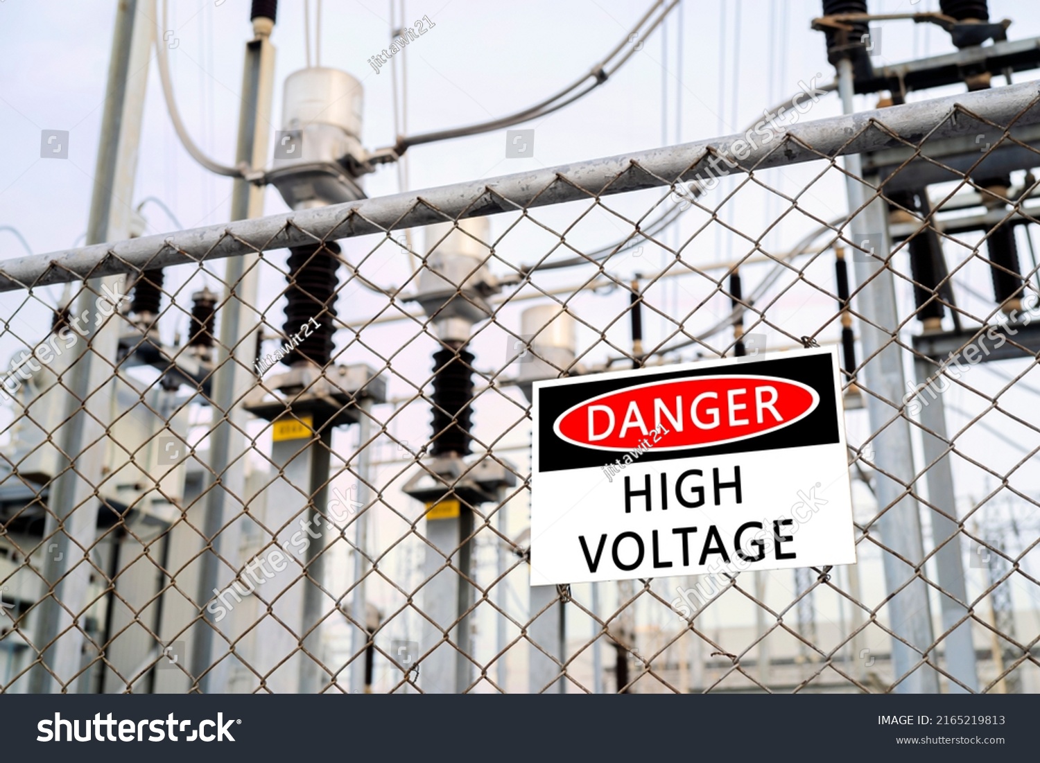 High-voltage transformer substation behind barbed-wire chain-link fence with Danger High Voltage sign. #2165219813