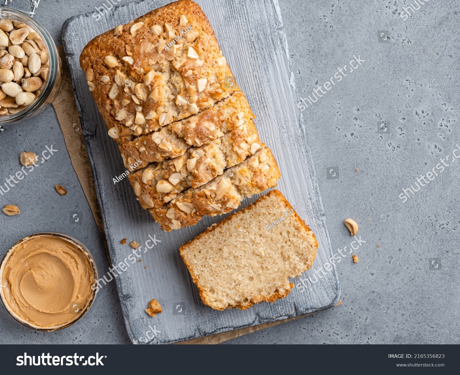 Loaf cake sliced on grey wooden cutting board. Homemade cake made of peanut butter, peanut flour and cinnamon decorated with chopped nuts. Top view. Copy space, gray concrete background. #2165356823