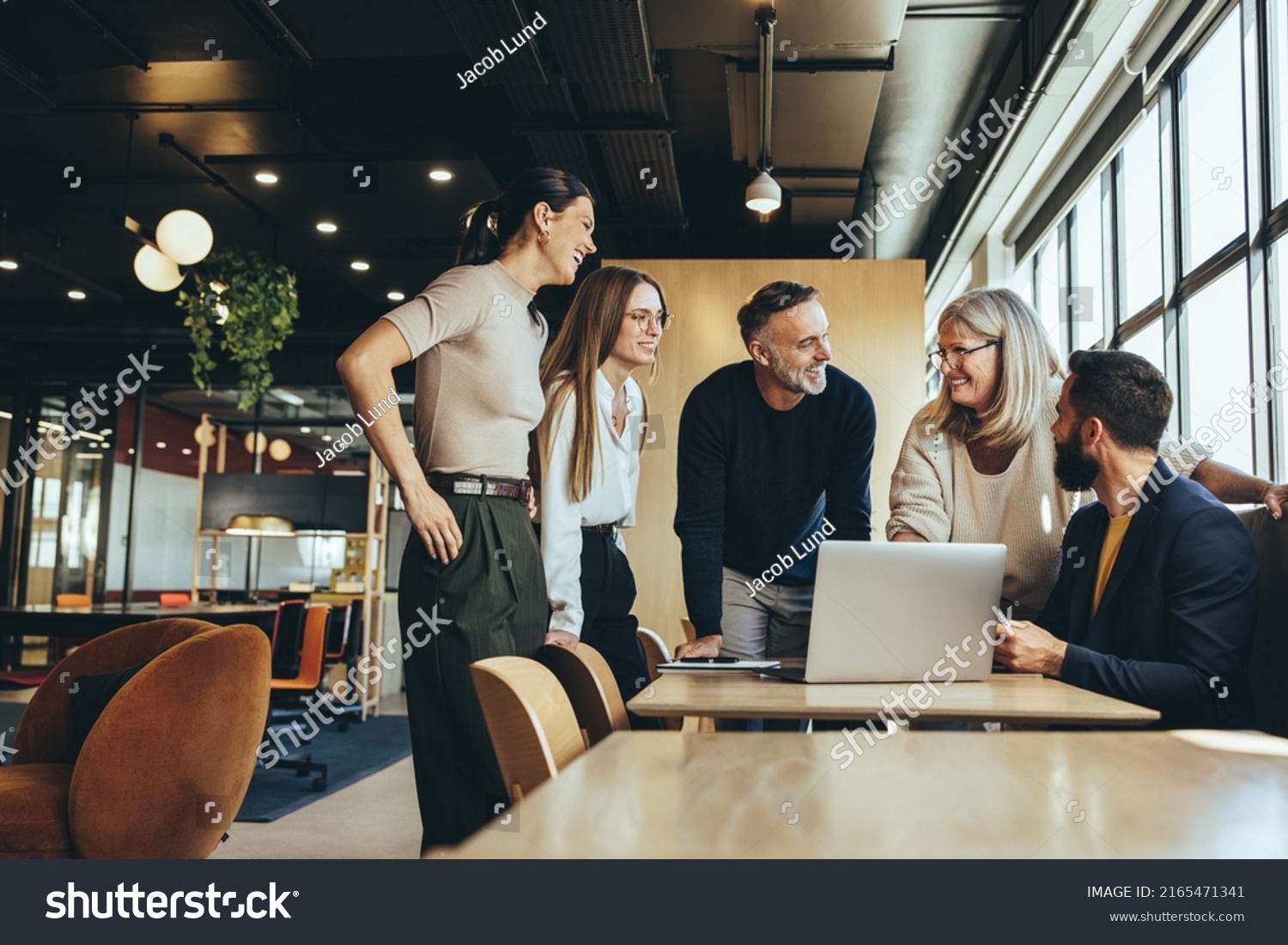 Smiling businesspeople having a discussion while collaborating on a new project in an office. Group of happy businesspeople using a laptop while working together in a modern workspace. #2165471341