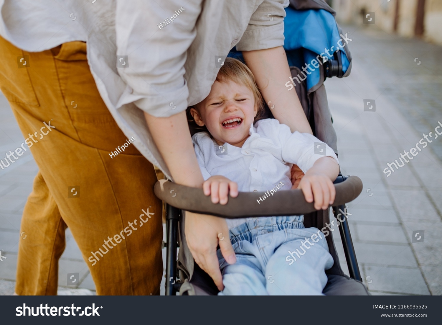 Mother calming a crying child sitting in a stroller while walking down the street #2166935525