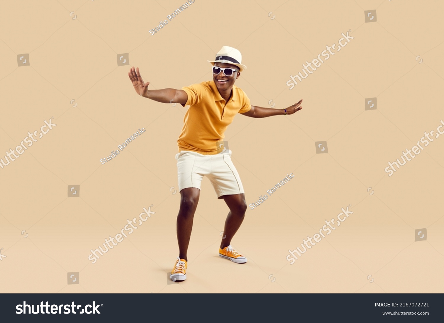 Cheerful stylish african american man having fun dancing on light beige background. Funny smiling dark skinned man in sneakers, shorts, polo shirt and hat with sunglasses. Full length. Banner. #2167072721