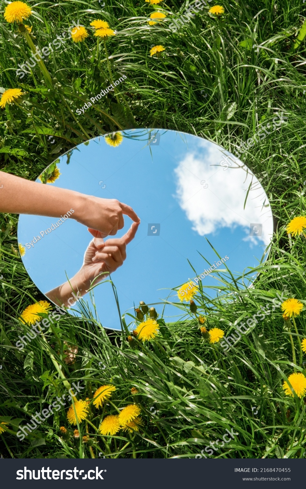 nature concept - hand touching sky reflection in round mirror on summer field #2168470455