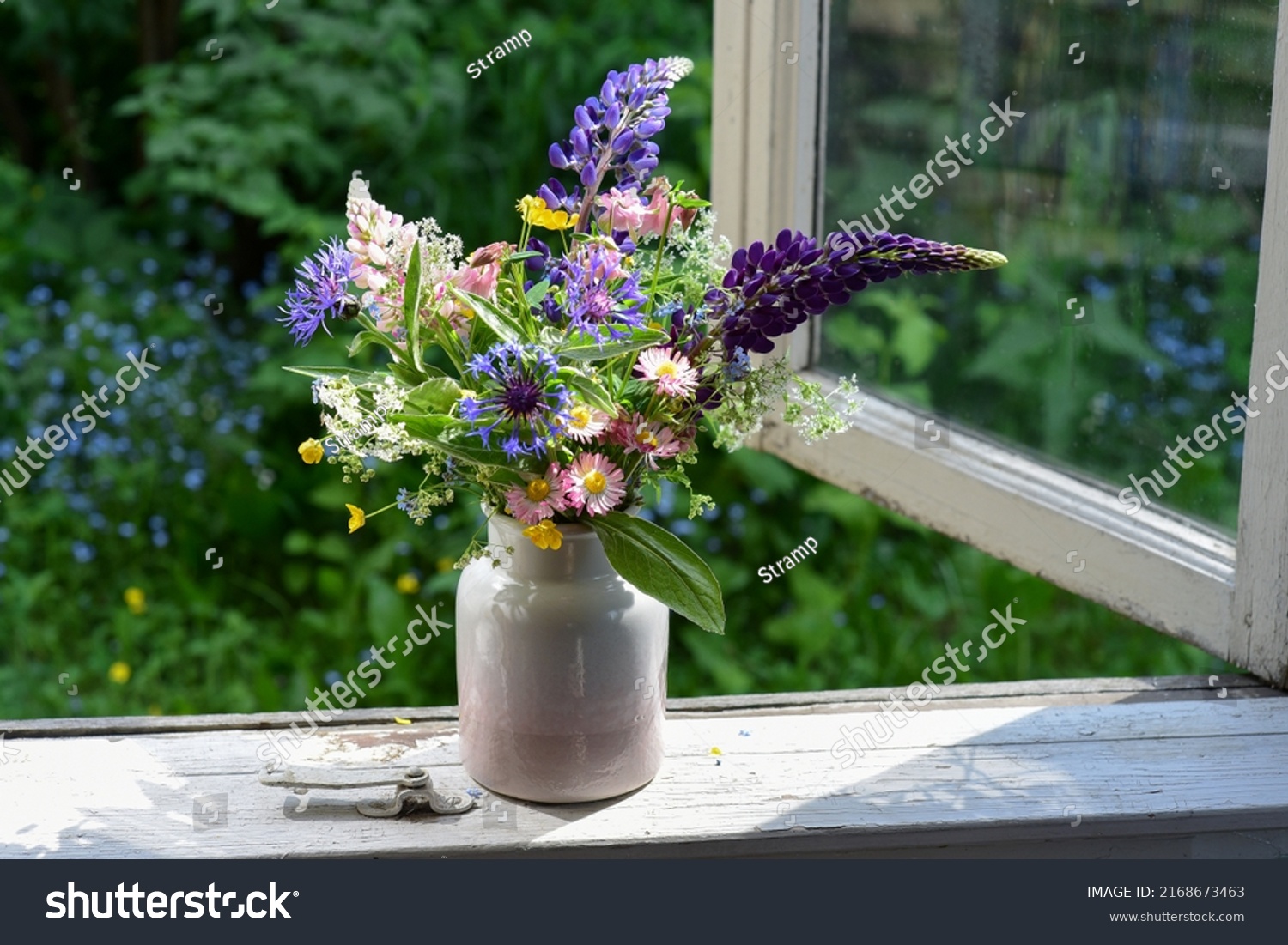 Bouquet of wild flowers in a vase on a wooden window sill. Still life on the window of an old country house, summer cottage. Floral home decoration.  #2168673463