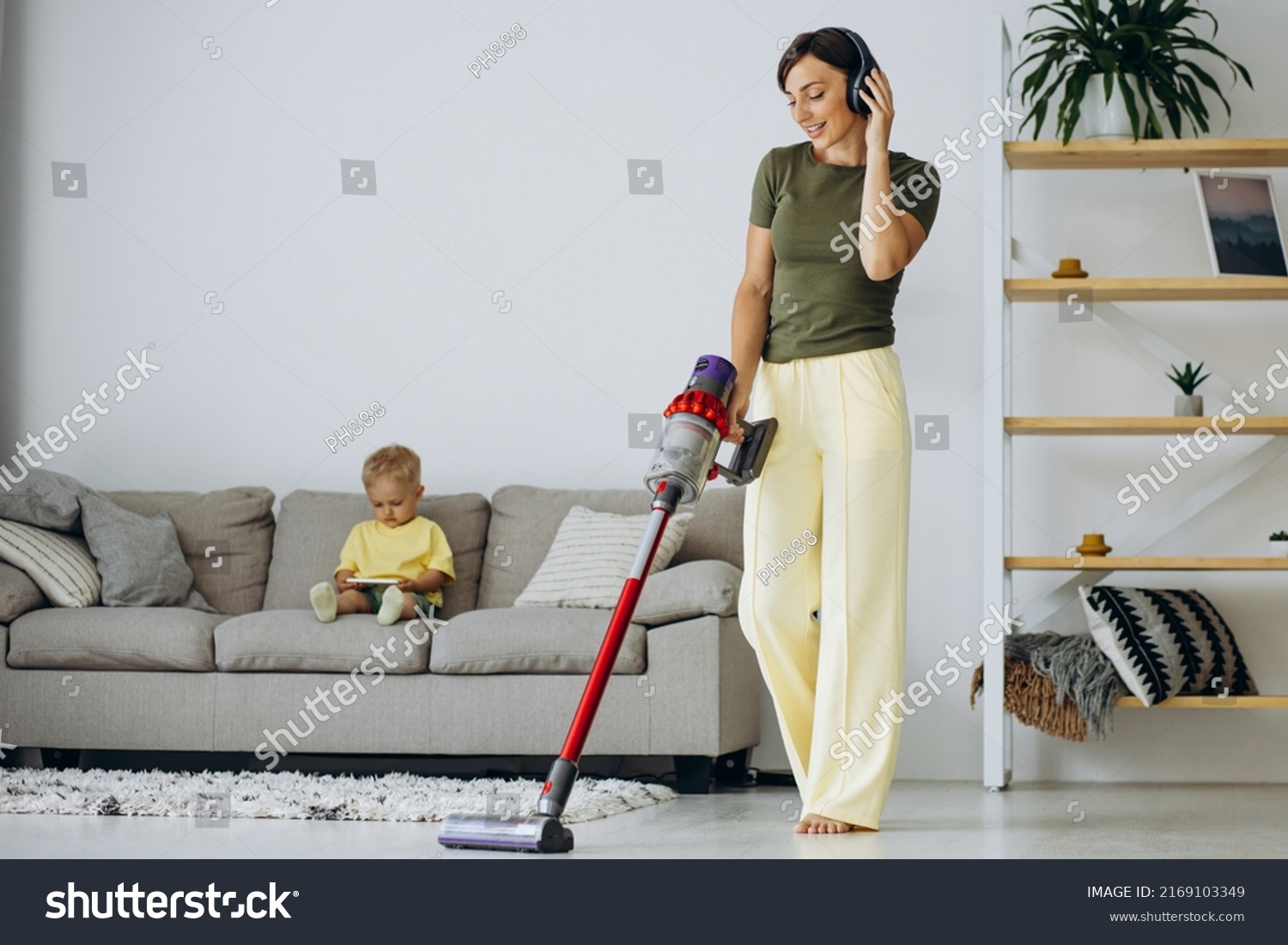 Woman vacuuming the house while little son sitting on sofa #2169103349