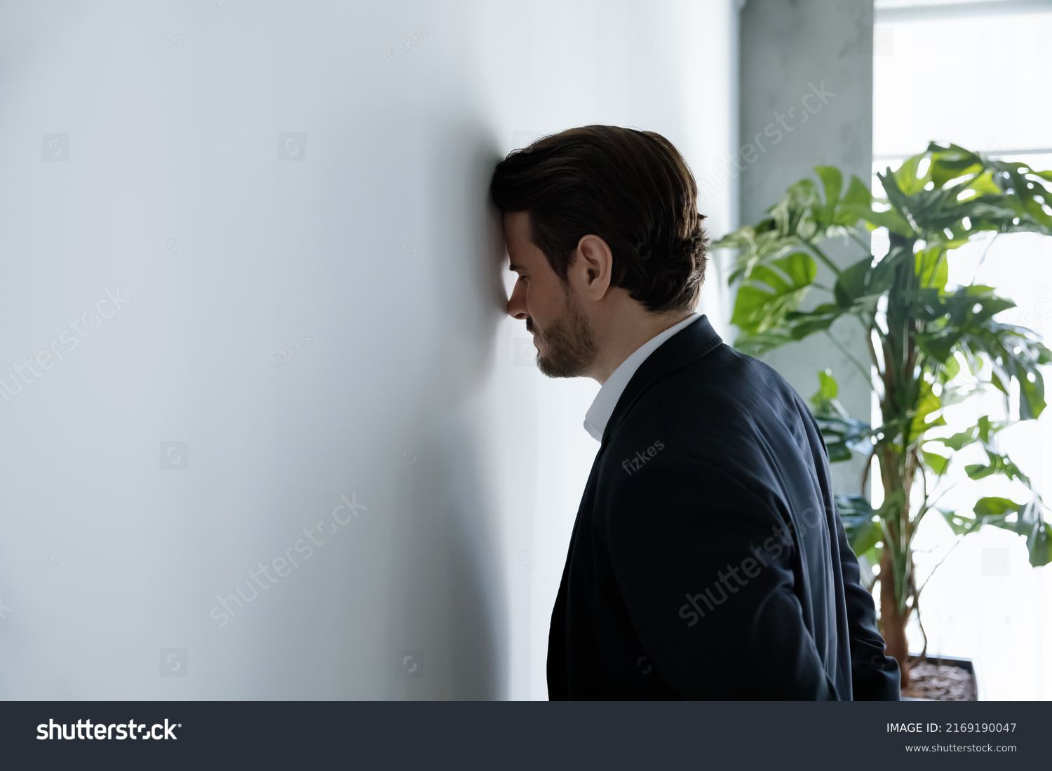 Upset businessman banging his head against wall in despair looks stressed having problems at work, bankruptcy, business failure unsuccessful negotiations, project loss, failed job interview concept #2169190047