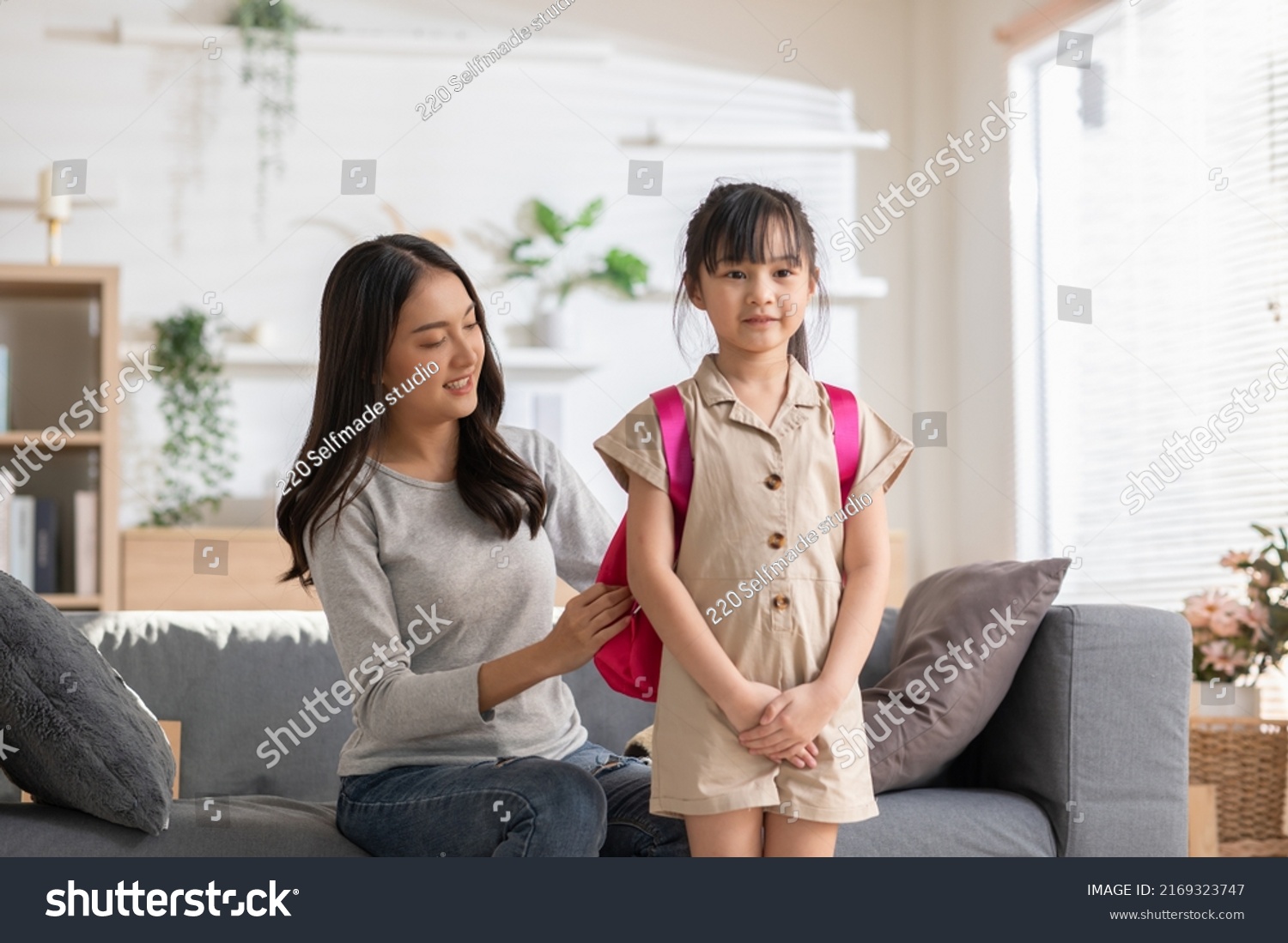 Asian mother preparing school bag of her daughter ready to school in morning. Happy mom helping her little girl get ready for school with love. First day to school. Good moment family. #2169323747