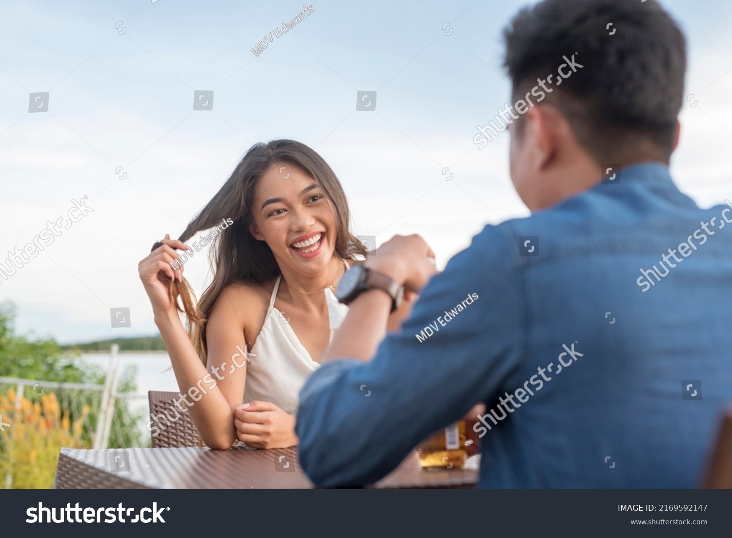 A young woman twirls her hair while listening intently to her date. Interested and attracted to a man she likes. A first date going well. Outdoor cafe scene. #2169592147