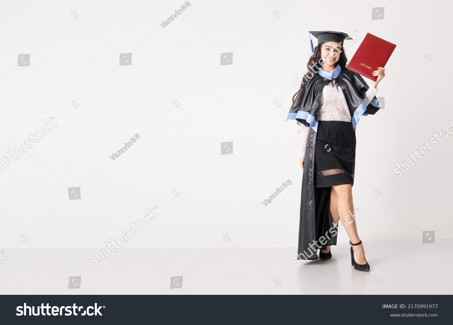 Woman student with diploma on white background with copy space. University graduate indian race woman wearing academic regalia and holding red diploma. #2170991977