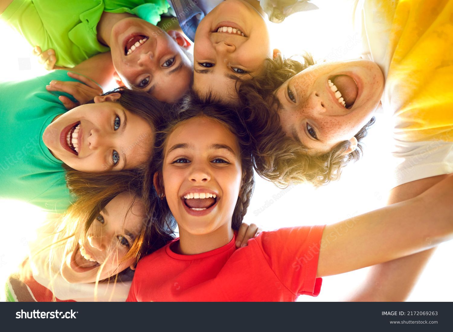 Bunch of cheerful joyful cute little children playing together and having fun. Group portrait of happy kids huddling, looking down at camera and smiling. Low angle, view from below. Friendship concept #2172069263