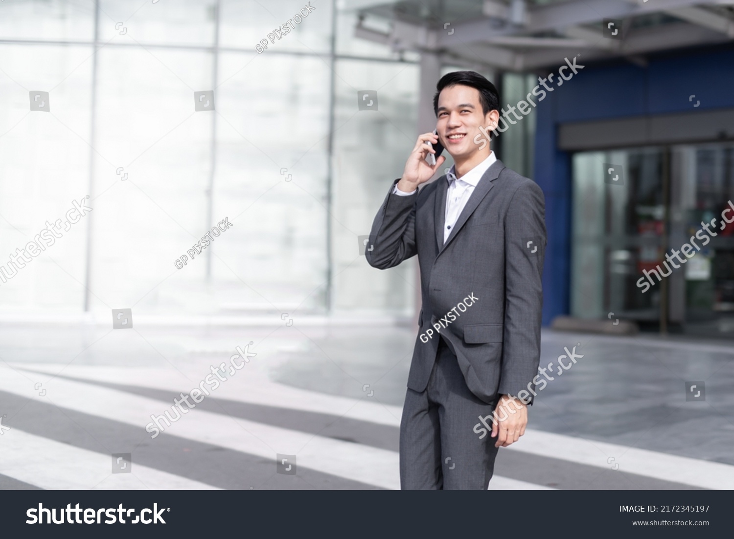 Asian Man with smartphone walking against street blurred building background, Fashion business photo of handsome man in casual suite with smart phone.  #2172345197
