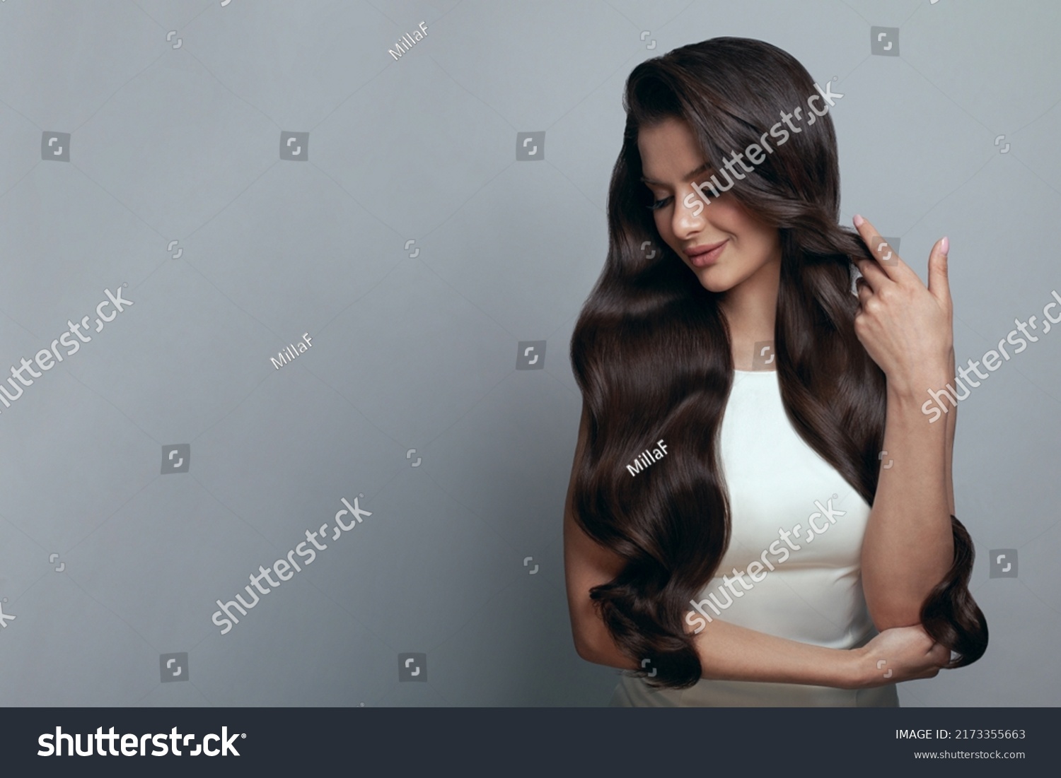 Portrait of elegant stylish young woman with long dark curly healthy shiny hair and makeup on grey banner background #2173355663