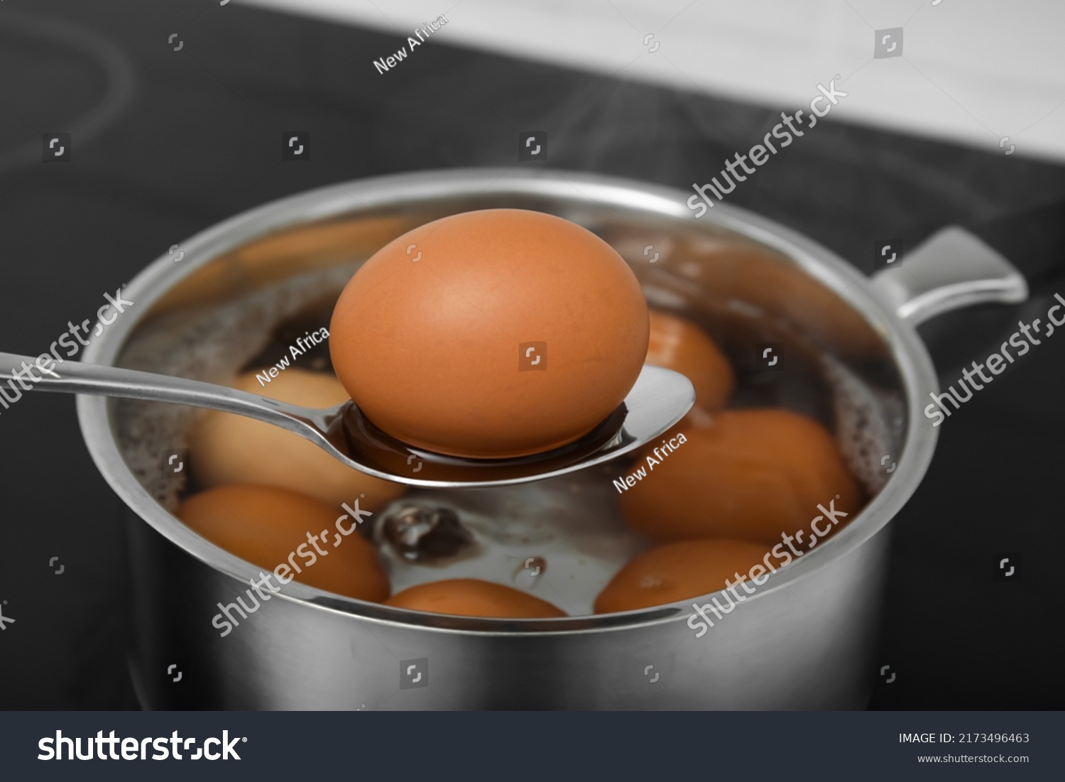 Spoon with boiled egg above saucepan on electric stove, closeup #2173496463