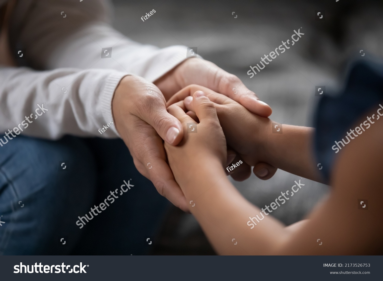 Close up compassionate young foster parent holding hands of little kid girl, giving psychological help, supporting at home. Sincere different generations family sharing secrets or making peace. #2173526753