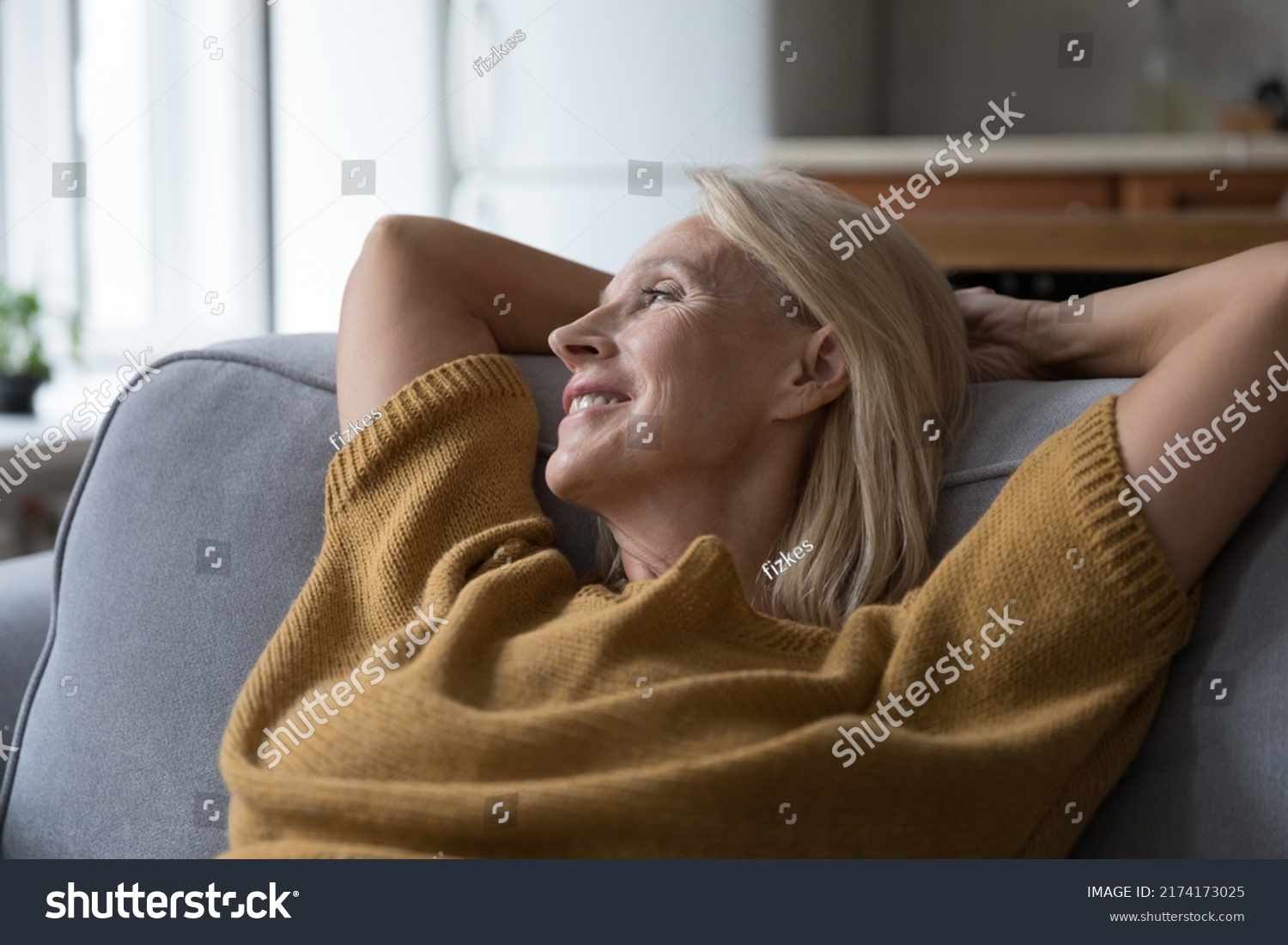 Close up older peaceful woman put hands behind head rest leaned on sofa cushions smile looks into distance, take break at home, enjoy fresh conditioned air inside. Hotel accommodation, relax concept #2174173025