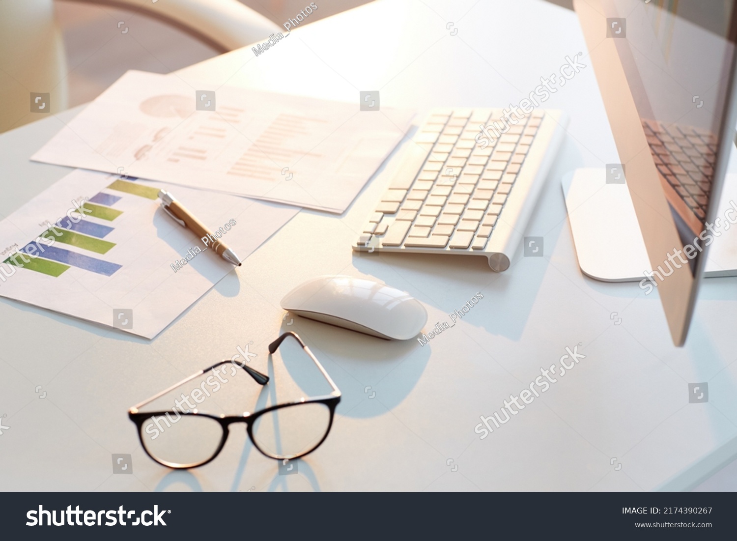 Close-up of business papers with graphs and charts placed on desk with computer, eyeglasses and pen, background #2174390267