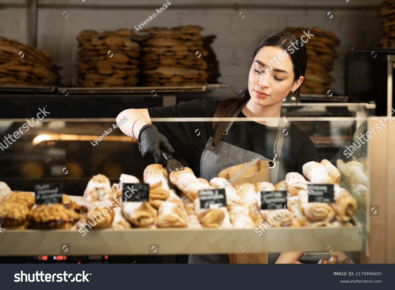 Cafe waitress girl puts fresh pastries on the cafe showcase, bread bakery worker #2174496605