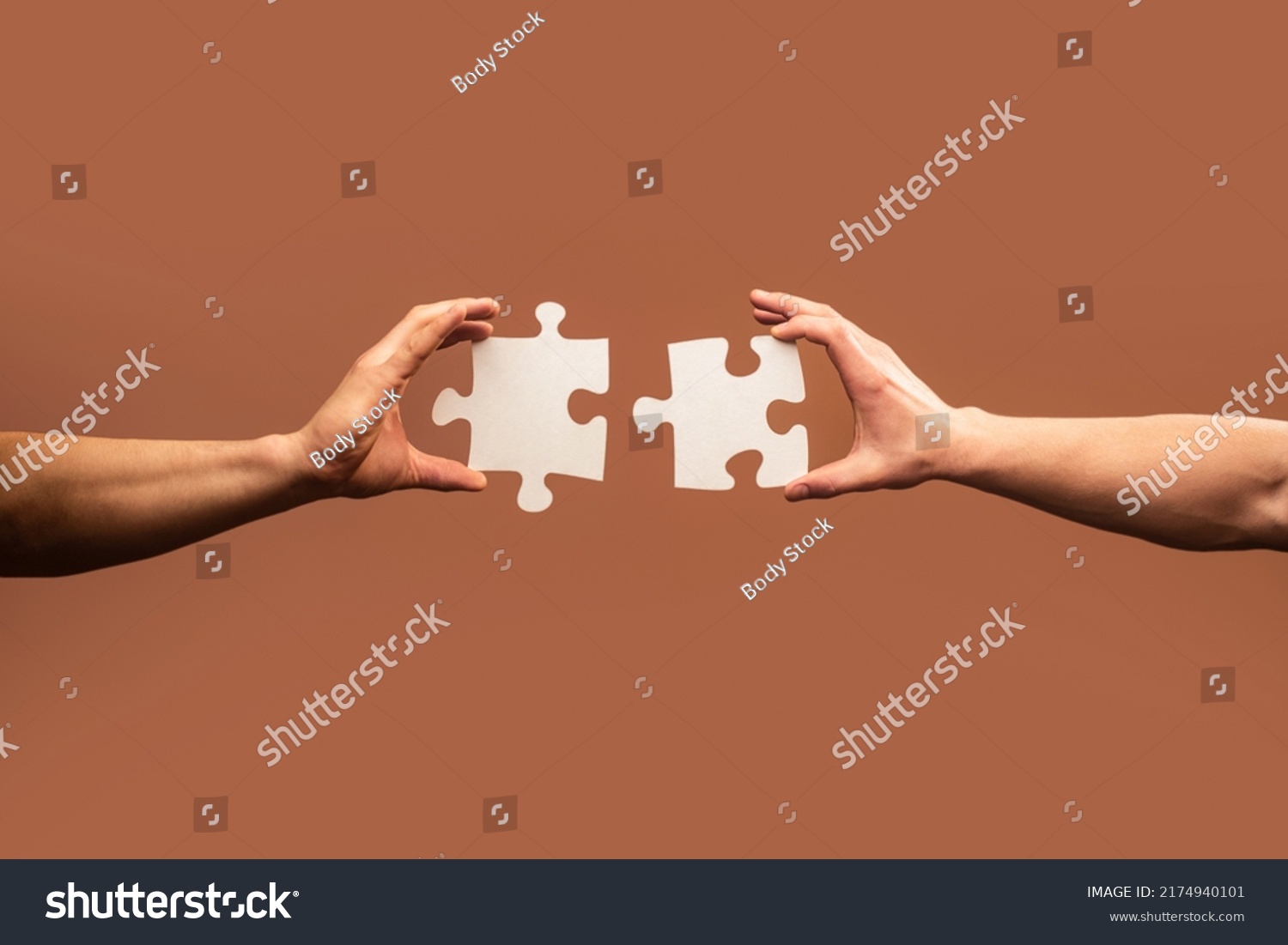 Two hands trying to connect couple puzzle piece on gray background. Teamwork concept. Closeup hand of connecting jigsaw puzzle. #2174940101
