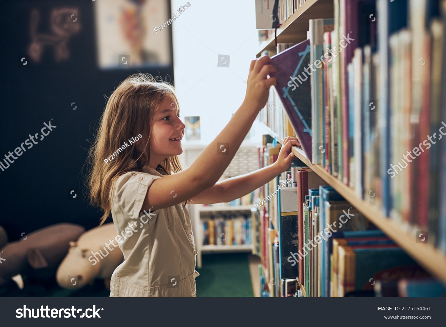 Schoolgirl choosing book in school library. Smart girl selecting literature for reading. Books on shelves in bookstore. Learning from books. School education. Benefits of everyday reading #2175164461