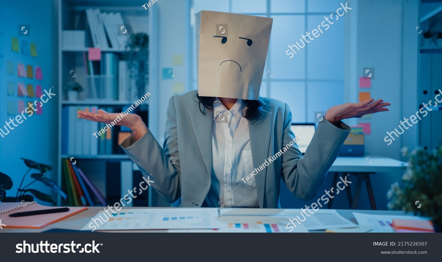 Young Asian businesswoman sit on desk wear draw sad mask paper craft bag feel bad mood with fail work project in office at night. Anonymous lady mad and confuse with overwork, Work mental health. #2175226507