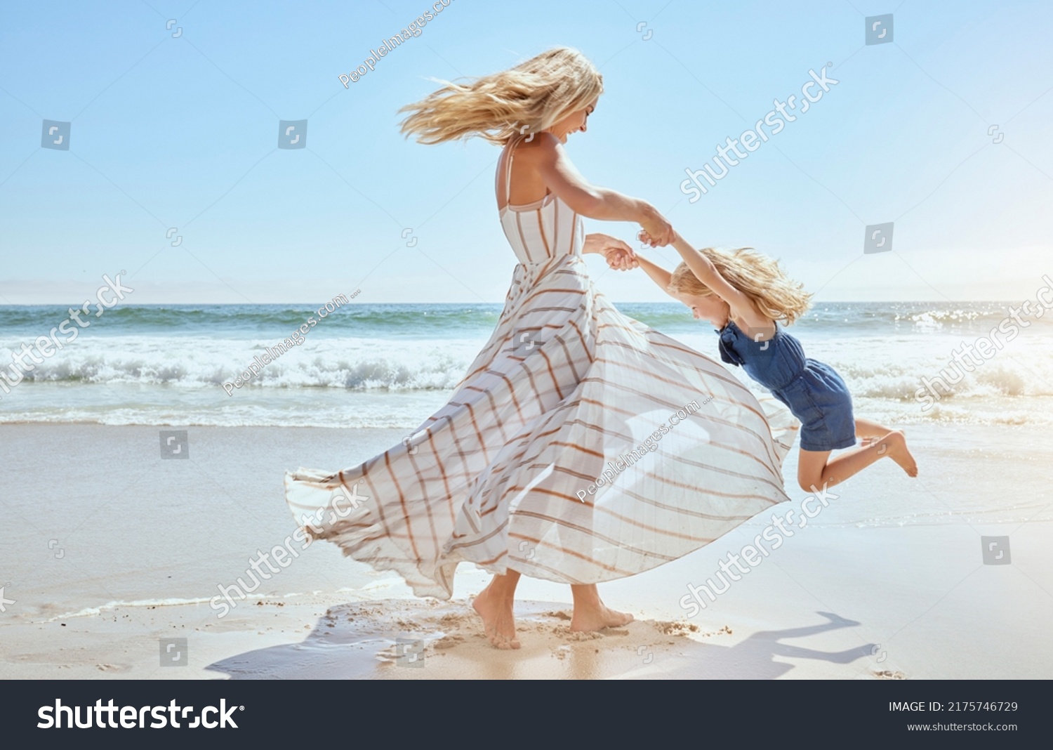 Happy mother swinging and spinning cute daughter in circles by the arms at the beach. Playful, energetic and joyful kid having fun while bonding with mom on sunny summer vacation outdoors #2175746729