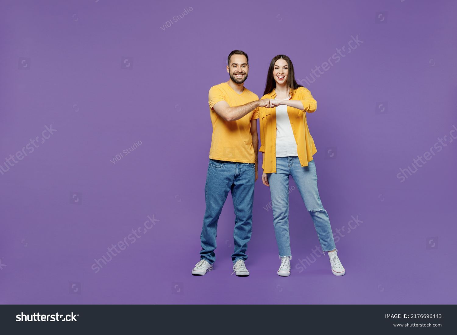 Full body young smiling happy couple two friends family man woman together in yellow casual clothes looking camera giving a fist bump in agreement isolated on plain violet background studio portrait #2176696443