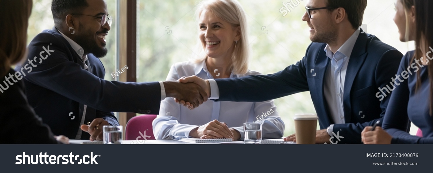 Banner image. African and caucasian millennial businessmen colleagues shaking hands on meeting in office, diverse enterpreneurs striking good deal, multiethnic teammates succeed in common project work #2178408879