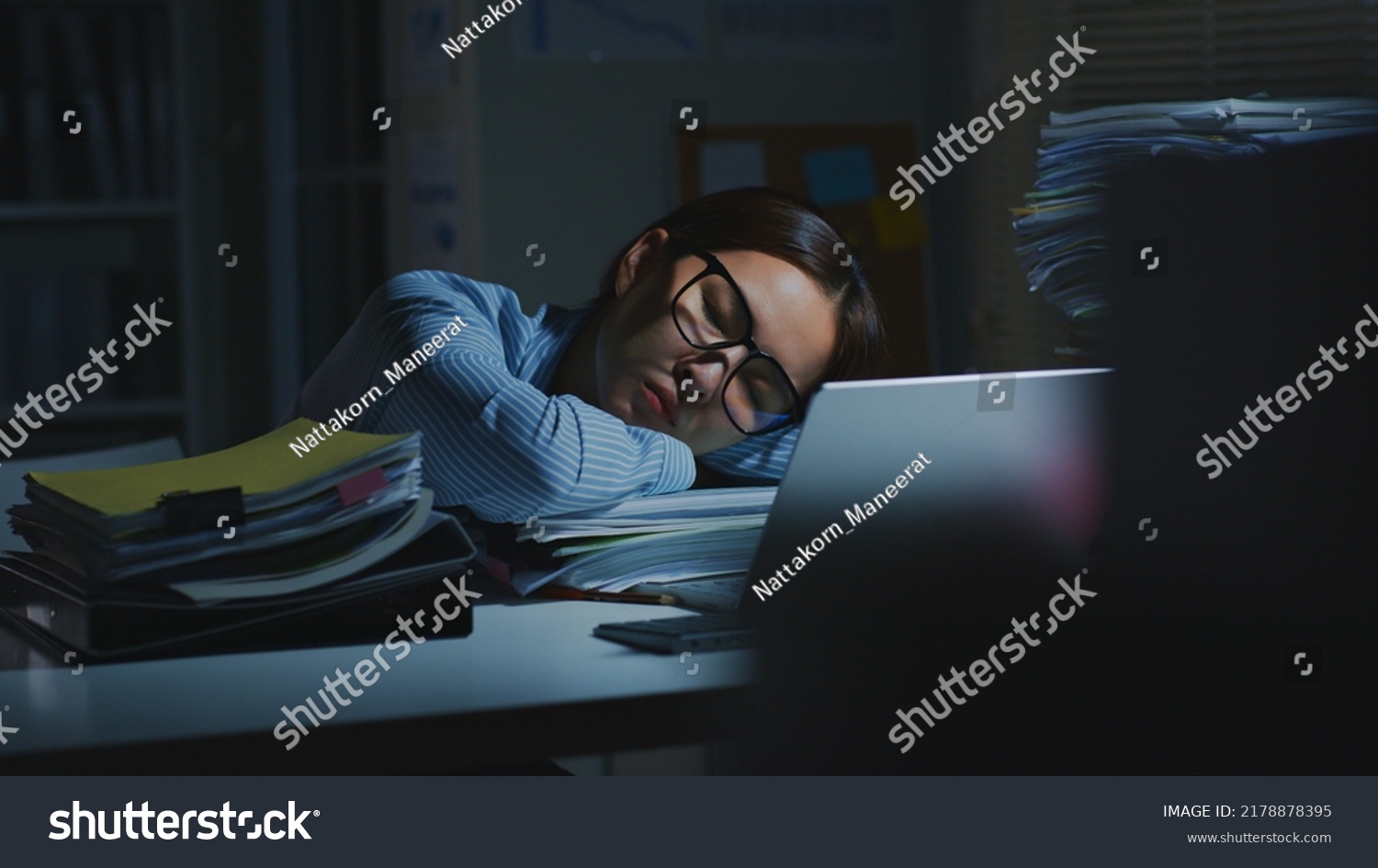 Overworked young Asian office employee sleeping while working on laptop computer overtime in office at night #2178878395
