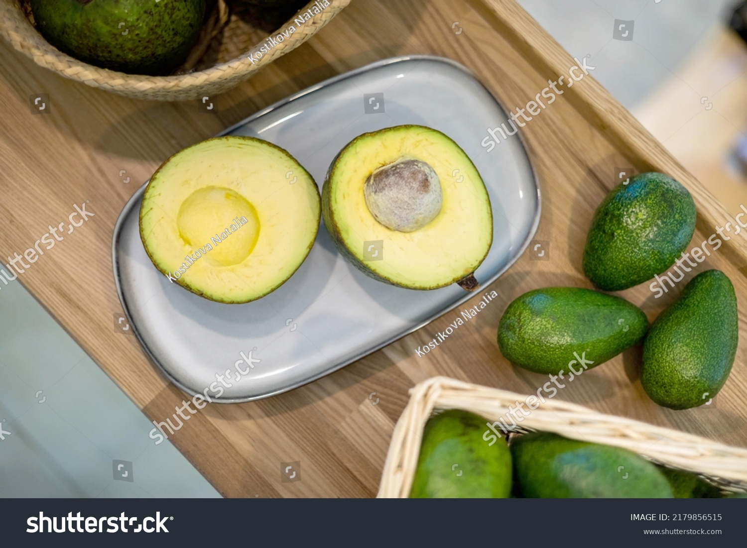Organic farm avocado in straw basket on wooden table closeup. Fresh ripe green exotic fruits full of healthy nutriment vegetarian eating. Three tropical edible plant with twig for guacamole cooking #2179856515