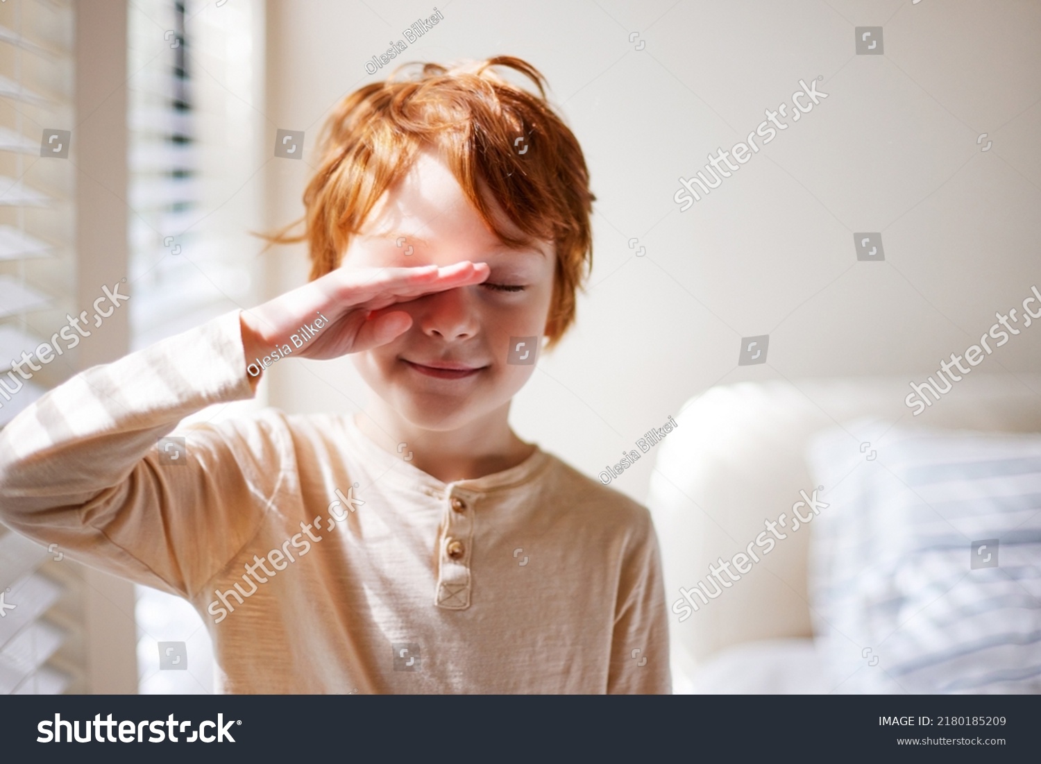 cute redhead young boy rubbing his eyes in the morning, waking up in sunlit bedroom #2180185209