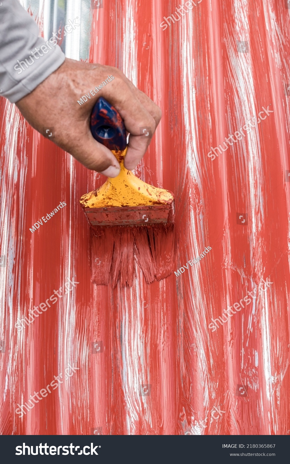 Painting the surface of a sheet of Galvanized Iron or GI corrugated metal with rust inhibiting red oxide primer. #2180365867