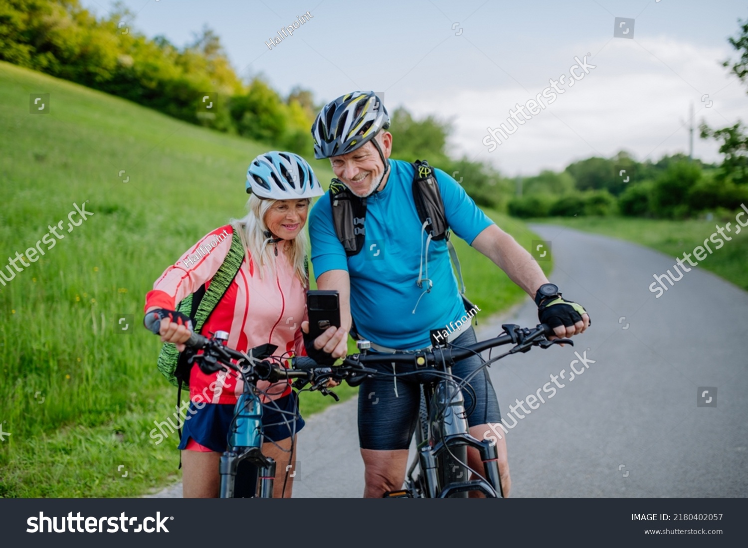 Active senior couple resting after bicycle ride at summer park, using smartphone. #2180402057