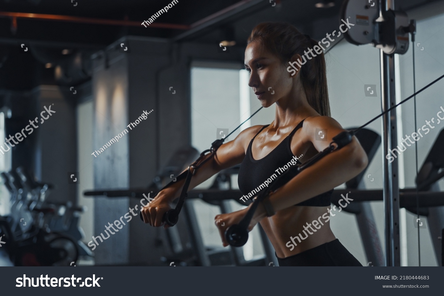 Sporty woman exercising on multistation at gym for arm and shoulders muscles. Fitness exercising in gym. #2180444683