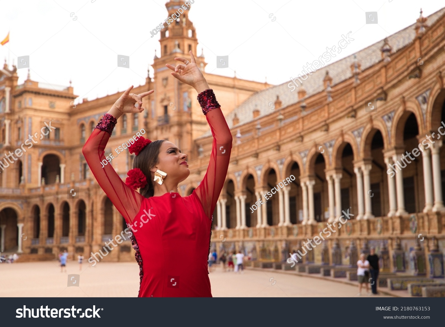 Beautiful teenage woman dancing flamenco in a square in Seville, Spain. She wears a red dress with ruffles and dances flamenco with a lot of art. Flamenco cultural heritage of humanity. #2180763153