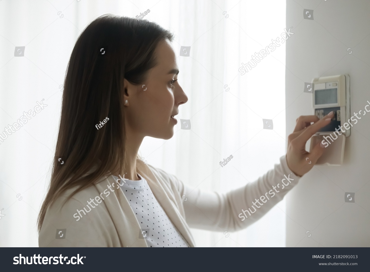 Millennial female client or customer switch turn on automatic smart home wall control panel. Young Caucasian woman regulate temperature or AC, using indoors house security system device. #2182091013